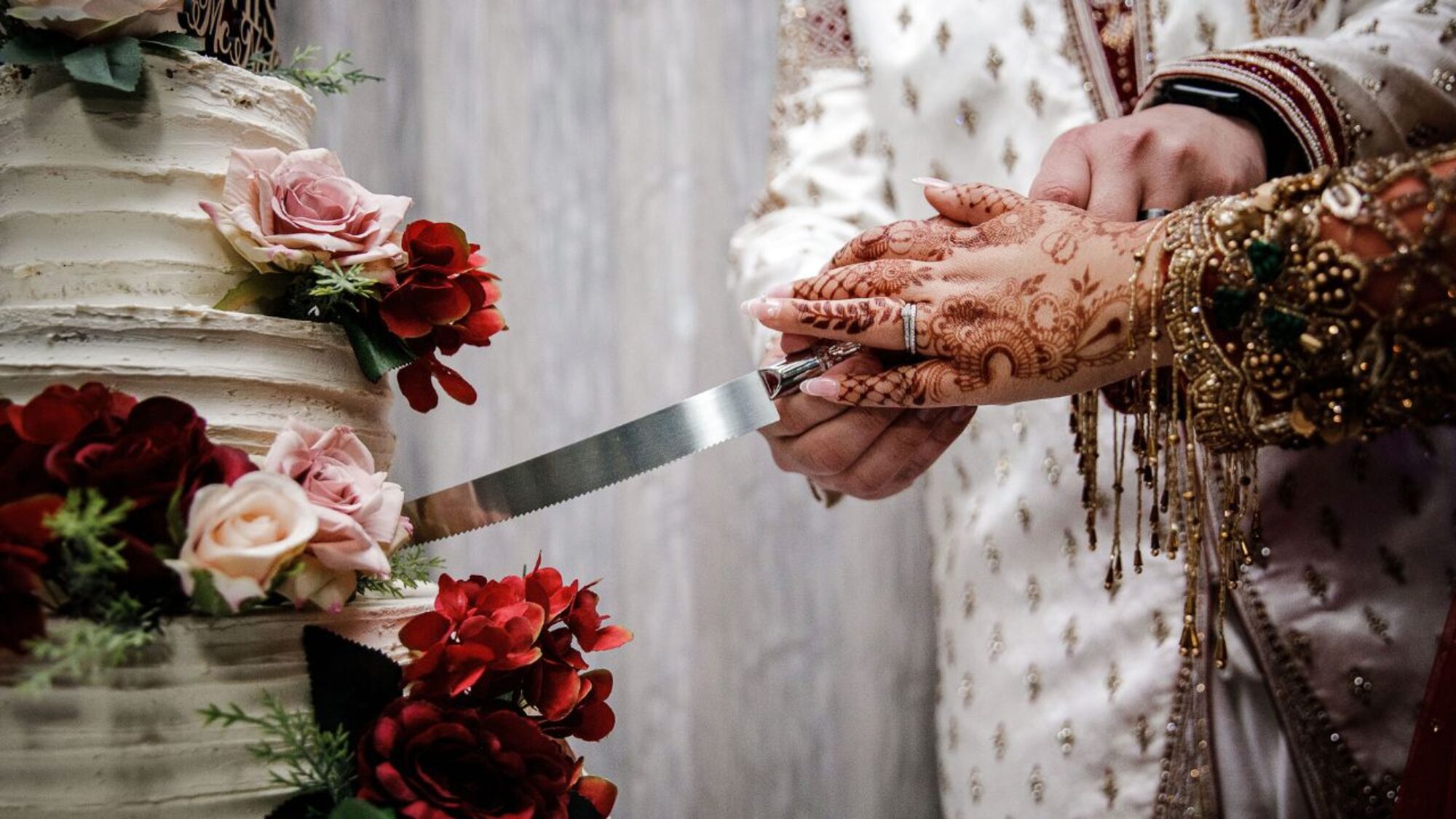 A couple on their wedding day cutting their cake, showing henna painted hands