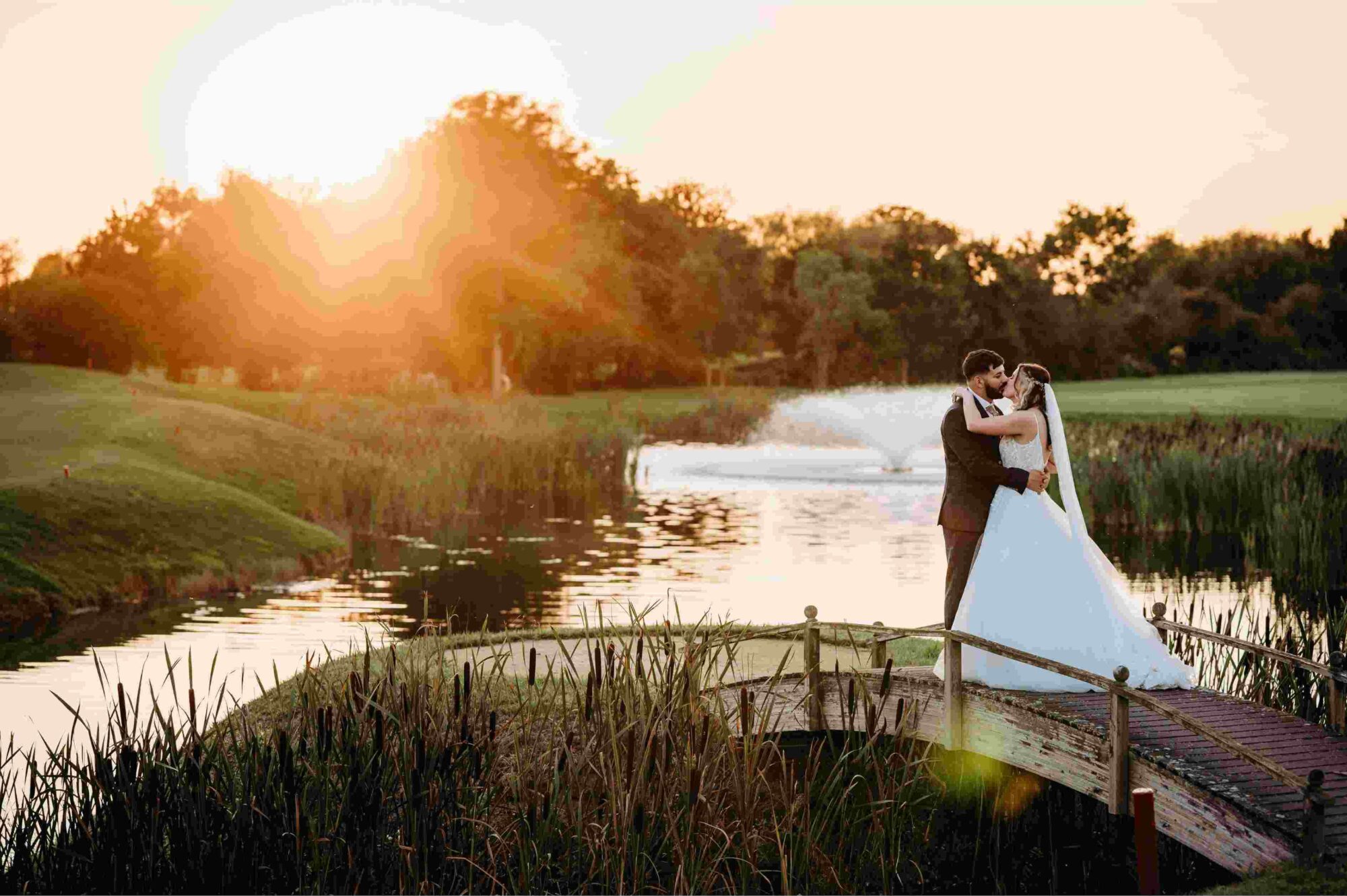 Married couple on their wedding on a scenic bridge on a gold course, kissing in the sunset